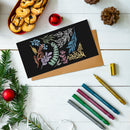 Decorative card with floral designs on a white surface with Christmas decorations and markers.