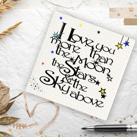 Card with 'I love you more than the moon, stars, sky' text on a textured surface with decorative elements.