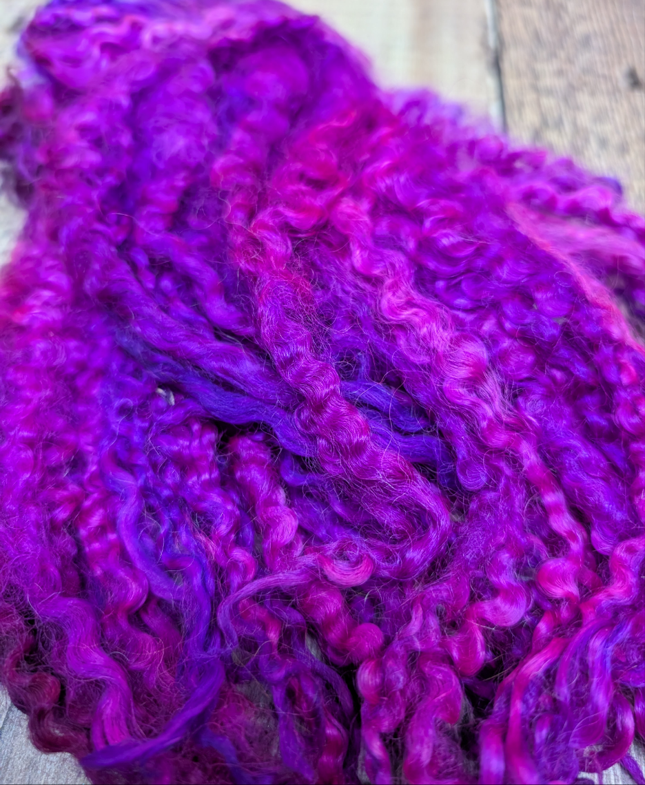 Close up image of a beautiful hand-dyed curly natural locks. This is a vibrant pink, purple colour