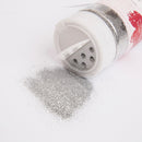 Silver glitter spilling out of a small container on a white background