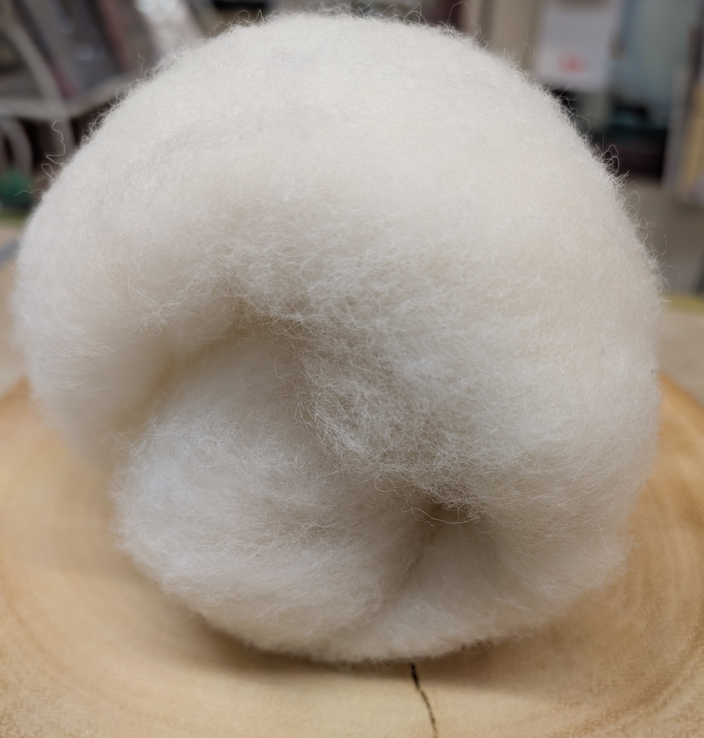 Ball of white wool on a wooden surface with a blurred background